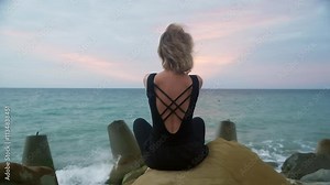 Young woman practicing yoga on the beach during sunset, raising her arms in a gesture of freedom and tranquility, with the serene sea creating a beautiful backdrop