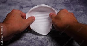 Men's hands first person view taking and putting protective face mask on camera white mask from threat like corona Covid-19 virus protects mouth and nose from dark black board capture in 4k 60fps