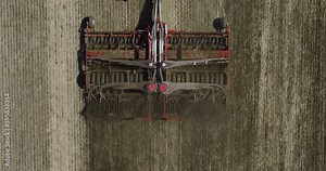 Field works. Tractor sowing seeds with seeder driller in field. Process of sowing cereals and other crops. Sowing work in the field. Tractor with seeder performing seeding. Top down drone view.