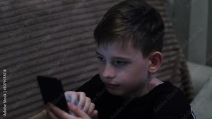 cheerful enthusiastic boy Caucasian 10 years old uses smartphone pressing on screen with fingers while at home, teenager spends time on social networks and messengers