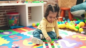 Adorable hispanic girl playing with maths puzzle game sitting on floor at kindergarten