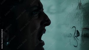 A detailed view of a persons horrified expression as they come face to face with a wall covered in ominous writing and drawings.