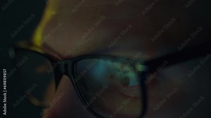 A monitor flickering in a dark office is reflected in the glasses of a programmer engrossed in late-night development. Using advanced technologies, program codes are created on a portable laptop