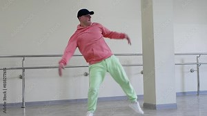 Modern youth breakdancing in the studio. Practice dance movements. Hip hop dancer. A young guy in a pink hoodie and light green hats.