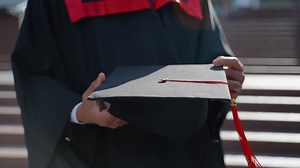 Graduate holding black hat with red tassel in hand