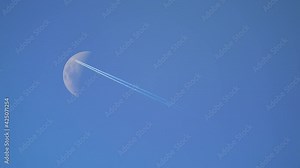 Plane Flies In Front Of Moon In daytime. Airliner flying high and moon. Contrail in blue sky.