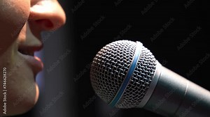 Close-up of woman high quality dynamic microphone and singing song or talking to people, on black background. Woman testing microphone voice for interview. Recording studio or concert.