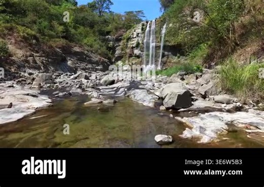 Sunlight illuminating cascading waterfall. Water flowing into rocky pool surrounded by lush greenery. Moss covered the cliffside walls Stock Video Footage - Alamy