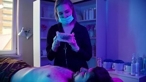 Waxing procedure - the master waxing the chest of her male client using a strip in neon lighting
