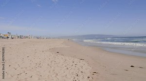 Low angle shot of empty sandy sea beach with waves crashing along the beach on the bright sunny day.