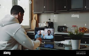 Multiracial colleagues working home on quarantine by making common video call by computer. Black man sitting in the kitchen and writing Stock Photo - Alamy