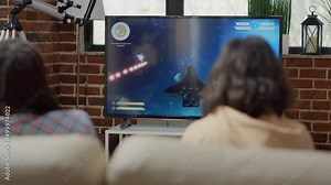 Cheerful people playing online video games on console cyberspace, using action shooting gameplay on television screen. Happy friends having fun with shooter competition at home.