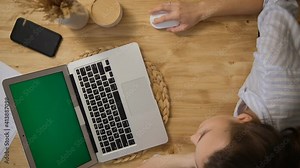Green computer screen. The girl lies at the table and remotely learns, works. A girl in a striped pajama top. Top view