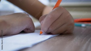 Child Holds a Pen in Hand, Writes Homework in a Notebook. Fingers compressing handle in a fist. Left-handed child. Distance learning at home. Performing lessons. Education concept, elementary school.