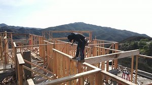 Worker hammering a beam in, standing on top of framing at a construction yard. High quality 4k footage