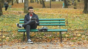handsome smiling happy man holding digital tablet using device laughing guy touching display tapping emotional cheerful face full view leisure autumn park bench communicate online social network wifi