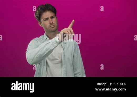 Man pointing index finger forward in studio against magenta wall, wearing white t shirt and denim shirt; concentration decision intent Stock Video Footage - Alamy