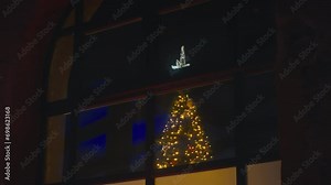 View through a large window of wonderful Christmas tree with a bright garland and decorations and a star. Beautiful decorated Christmas tree outside the store window in the evening before the New year Stock Video