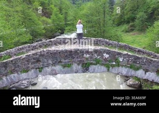Blonde woman crossing historic stone arch bridge above forest river travel heritage detail. Female tourist walks woodland stream ancient masonry green valley summer water landscape texture. stone bridge, historic bridge, female traveler Stock Video Footage - Alamy