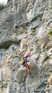 Climber going down with a rope after creating a new climbing route by using rock drills and rotary hammers on the climbing rope. Climber wears a red helmet.