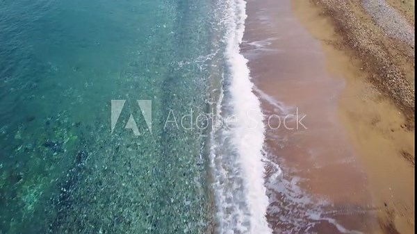 Drone view captures waves along beach, sandy surf meeting sea. Beach's sand greets rolling waves, drone overhead. Sea waves crash onto beach sand, drone soaring above