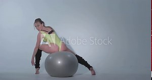 Beautiful girl sits on a ball a back to us, a yellow sports suit and black leggings, she is engaged in gymnastics on a gray rubber ball, swimsuit, beautiful skin, figure, barefoot, long hair