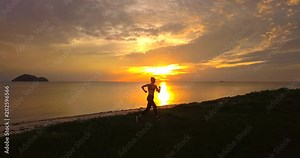 Running athlete woman jogging at sun sunset beach. Fitness runner girl training outside by the sea coast line in beautiful sunset or sunrise in full body length in summer time,tracking shot