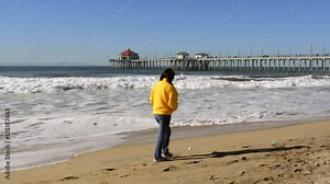 A woman walks along the shoreline at historic Huntington Beach pier in Orange County California during a cold, windy day..