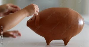 Close-up hands adding coins inside piggy bank investment
