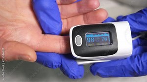 Doctor examining patient with fingertip pulse oximeter, close up. Pulse oximeter on patient finger showing low oxygen saturation. Medic and patient using finger pulse oximeter.