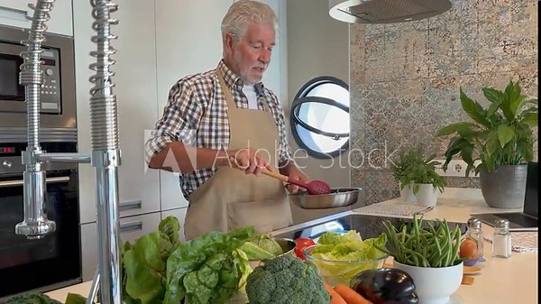 Man at home cooking vegetable in a pot with a table spoon. People in the kitchen preparing dinner. One mature male alone cooking. Real lifestyle person testing taste and cook preparation