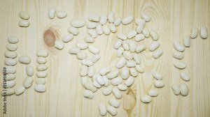 Moving white large beans forming the word BEANS with letters and transform to figures of a plate and spoon. Stop motion animation on a wooden table.