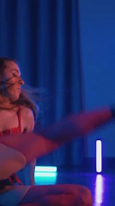 Vertical. Young woman in red lingerie erotically dancing twerk and high heels. Half-shaven Girl in black shorts moving seductively gracefully in darkened space. Striptease in a disco club on stage.