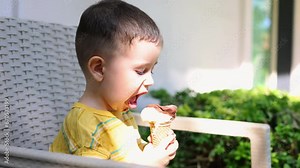kid boy and baby eating ice cream in cone sitting on chair outdoor balcony garden terrace on park bench. cute siblings enjoying food outside. ice cream is melting, summer, vacation in hotel.