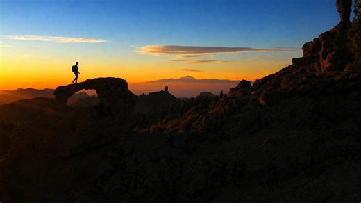 Hiker crossing a natural stone arch at sunrise