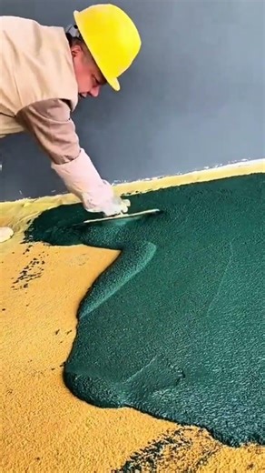 applying green rubber flooring material carefully on a yellow base using a specialized metal tool