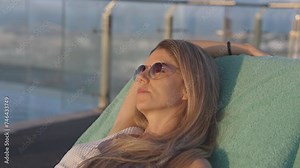 Woman sunbathing next to a luxury outdoor pool during sunset Stock Video