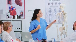 Doctor describing the layout of the human spine in front of colleagues using skeleton model explaining medical procedures standing in hospital office. Physicians discussing about symptoms of disease