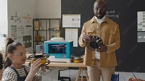 Zoom out shot of African American teacher giving filament spool to school kids and explaining how to use it during 3D printing lesson Stock Video