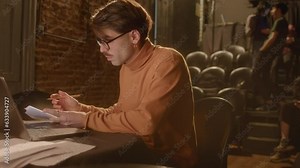 Professional playwright typing on laptop and making notes on papers while working on theater stage. Medium handheld shot Stock Video