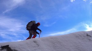 Climber with large backpack using an ice ax goes on a snowy ridge