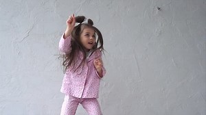 Happy young girl having fun in bedroom. Jumping and playing on bed. Girl in pink pajama.