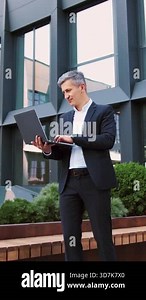 Handsome older man entrepreneur using laptop remotely computer for online business. Focused mature successful businessman working, scrolling, typing on laptop sitting outdoors at office building