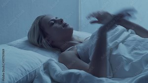 Young woman lying in the bed at night and having insomnia disease. Beautiful blond sleeping girl. Twilight in the bedroom, moonlight from the window. Sleeplessness concept.