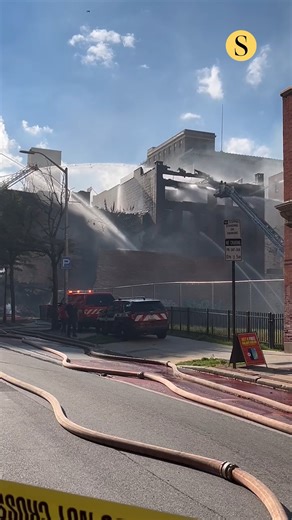 Baltimore firefighters are battling a five-alarm fire in a building at the intersection of North Howard Street and West Fayette Street on Tuesday afternoon, according to the Baltimore City Fire Department. Three structures have been affected, including two four-story buildings and one smaller building that has collapsed. The Maryland Transit Administration has shut down the light rail in the vicinity of the fire with train service suspended between Patapsco and Falls Road. Commuters should use s