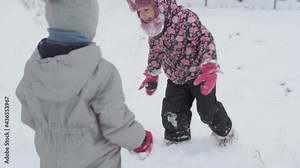 vacation, game, family concept - slo-mo authentic Two happy preschool toddler kids siblings slide down the hill and help each other climb up. snowfall in cold season weather in winter park outdoors