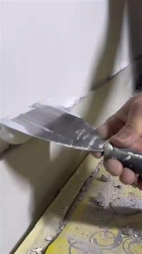 Spreading wall filler with putty knife and smoothing surface during indoor repair work task