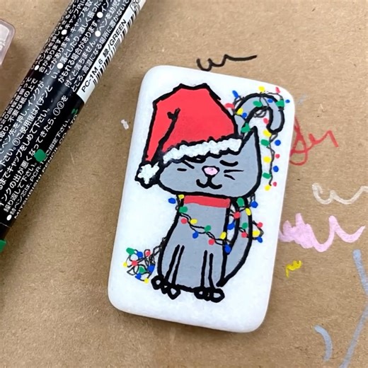 We LOVE Christmas Kitty ❤💚 Combination of Posca paint pens and a Micron pen for the lights! Comment "shop" if you need supplies! Check out more from our Winter - Holiday - Christmas Rock Painting Ideas - https://www.facebook.com/1511584975583999/playlists/2338745503245426 *It is important to know how to seal your rocks when using ink and paint pens. Comment "how to seal rocks" if you need that information* | Rock Painting 101