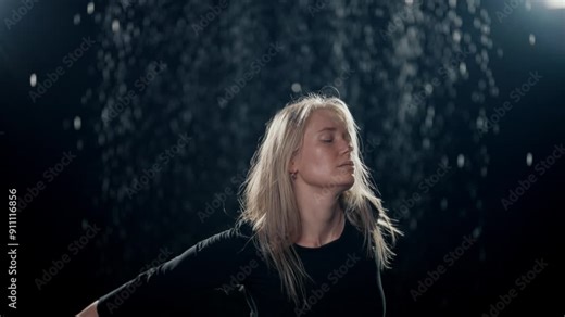 Beautiful blonde woman dancing in night in rain or snow, medium female portrait . Graceful ballerina moving hands slowly in dark studio, romantic and fabulous shot with talented female dancer, hobby