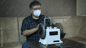 Masked asian man sharpens knives on a grinder